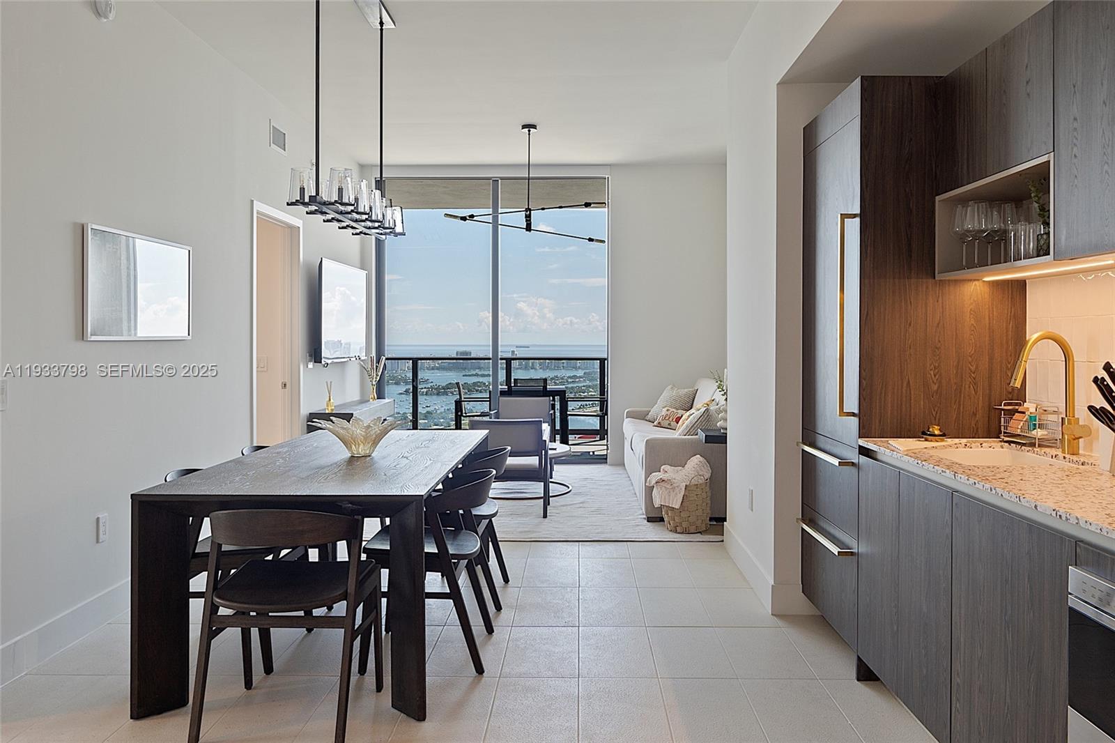 A modern kitchen and dining area overlook a living room with a balcony and water view — 159 NE 6th St # 5015, Miami FL 33132, MIAMI, FL