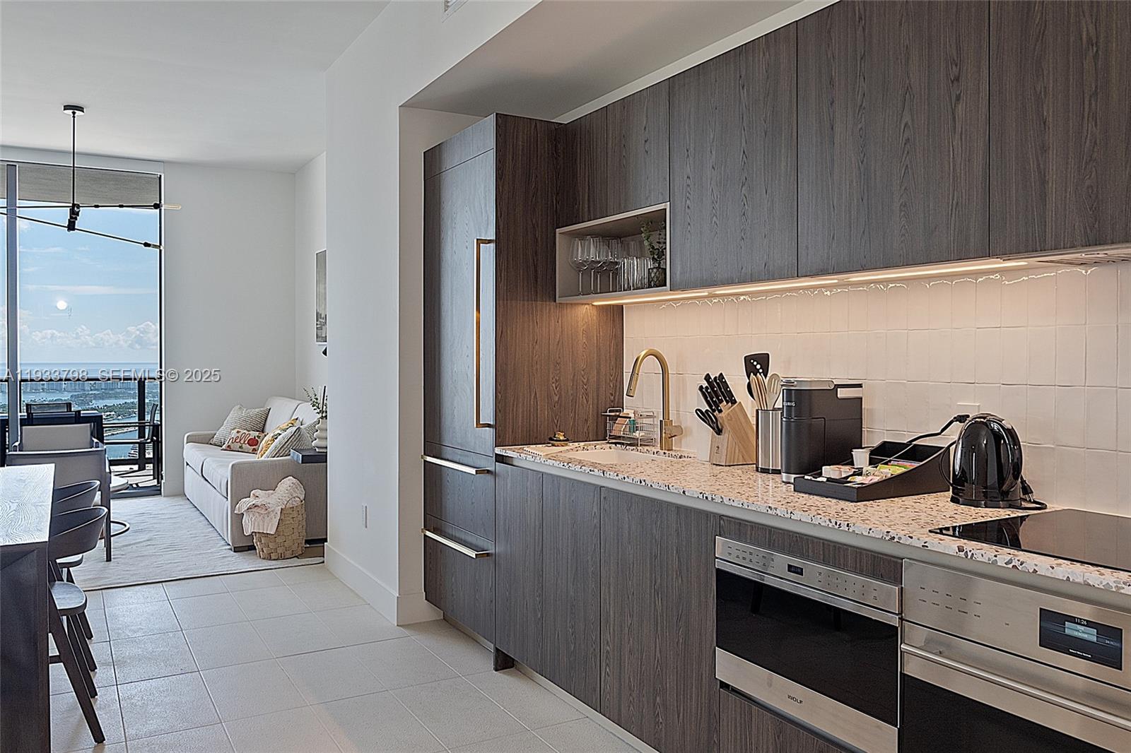 A modern kitchen with dark wood cabinetry, speckled countertops, and an adjacent living area — 159 NE 6th St # 5015, Miami FL 33132, MIAMI, FL