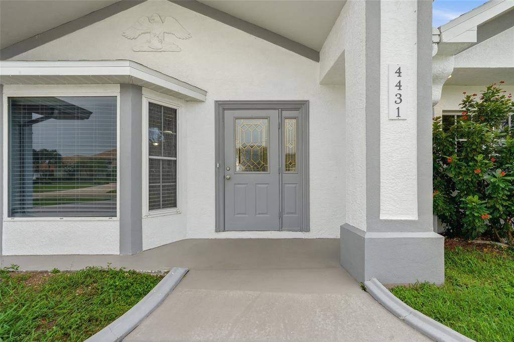 The exterior of a house features a gray front door, a concrete walkway, and white walls — 4431 SE 19TH AVENUE, CAPE CORAL, FL