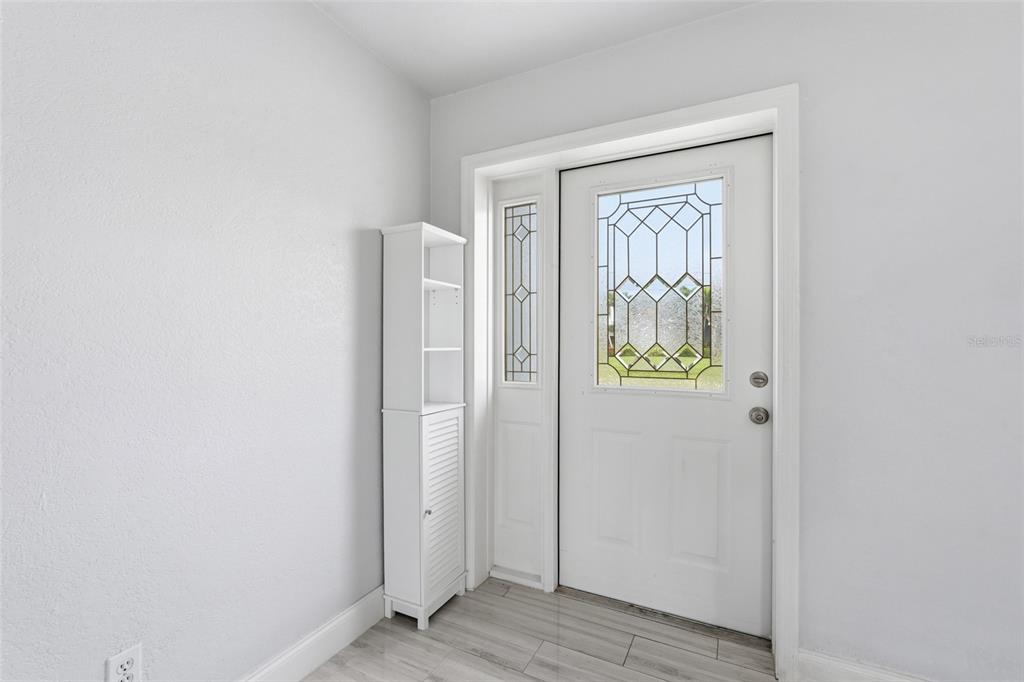 A white front door with a decorative glass insert stands next to a tall white cabinet — 4431 SE 19TH AVENUE, CAPE CORAL, FL