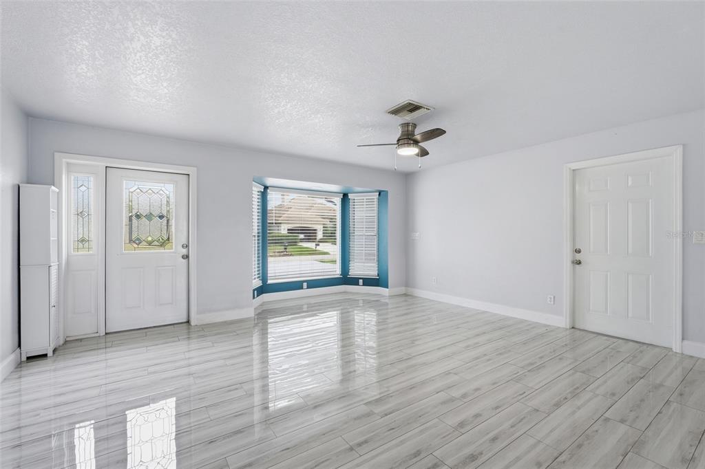 A bright living room features light gray walls, wood-look tile flooring, and a bay window — 4431 SE 19TH AVENUE, CAPE CORAL, FL