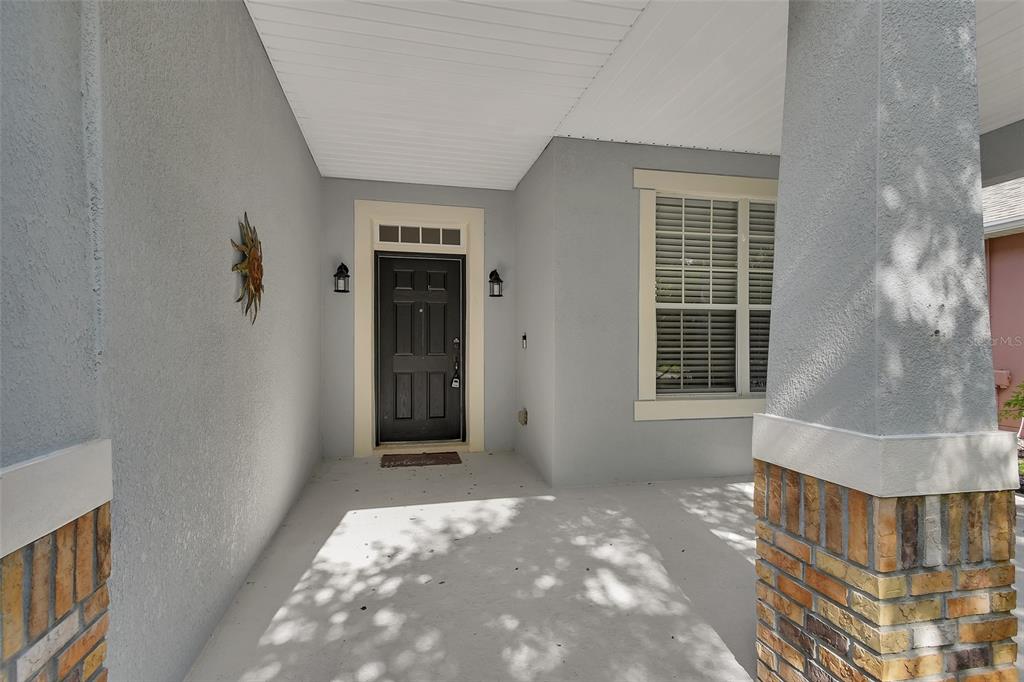 A covered front porch features a black door, light gray walls, and brick-accented columns — 525 HERON POINT WAY, DELAND, FL