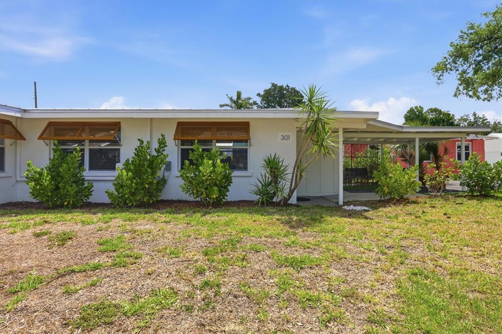 A white single-story building features a covered entryway, wooden window awnings, and landscaped shrubs — 301 28TH STREET W, BRADENTON, FL
