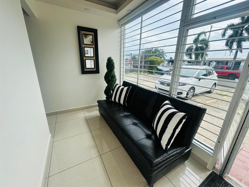 A black sofa with striped pillows sits in a room with large windows and tile floors — 1396 CALLE BONITA, PONCE, PR