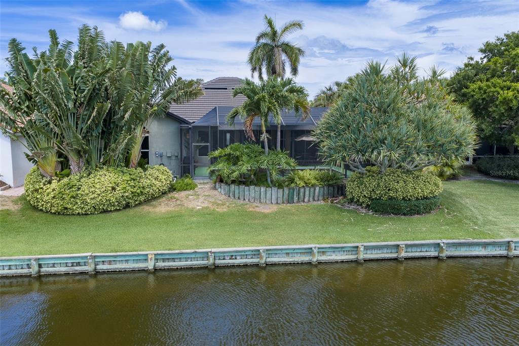 A waterfront house features a screened-in patio, lush tropical landscaping, and a wooden seawall — 4834 WINDMILL PALM TERRACE NE, ST PETERSBURG, FL