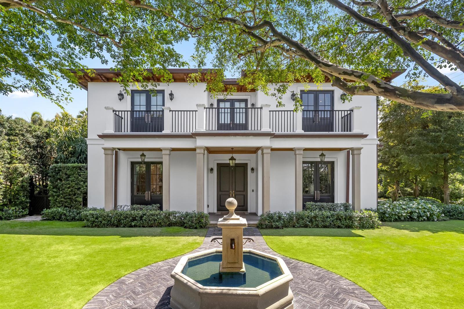 A two-story white house with a balcony, dark-framed doors, and a stone fountain in front — 1053 N Lake Way, Palm Beach FL 33480, PALM BEACH, FL