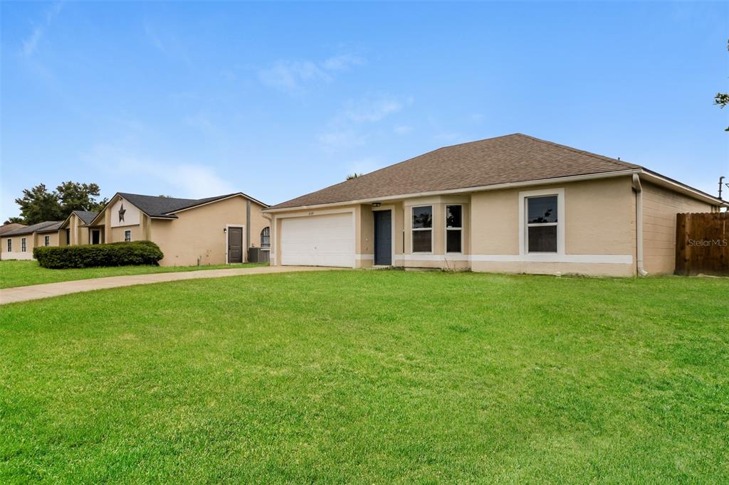 A single-story house with a tan exterior, a white garage door, and a large lawn — 2729 GRAMERCY DRIVE, DELTONA, FL