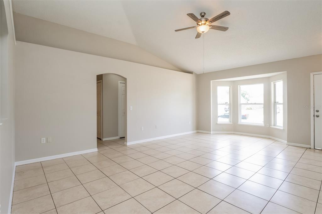 A living room with beige tile flooring, vaulted ceilings, a ceiling fan, and a bay window — 2729 GRAMERCY DRIVE, DELTONA, FL