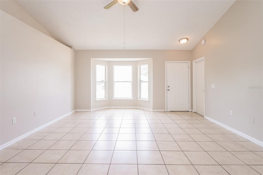An empty room with beige walls, tile flooring, a bay window, and a ceiling fan — 2729 GRAMERCY DRIVE, DELTONA, FL