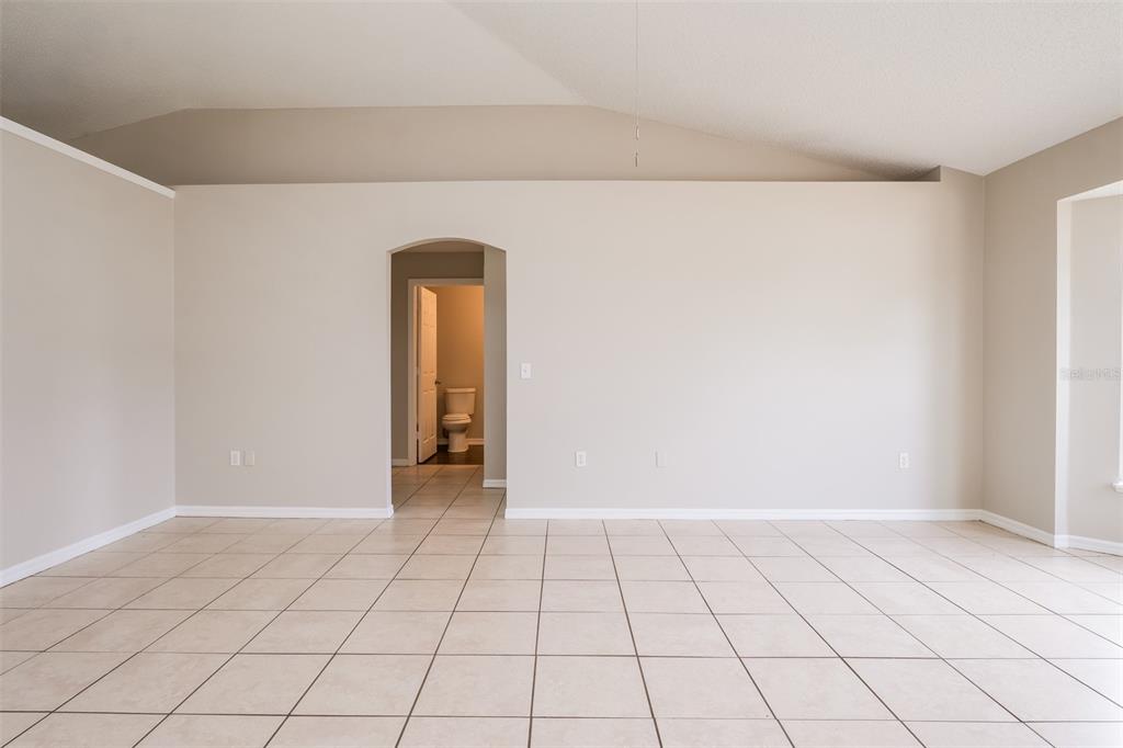 An empty room with beige walls, tile flooring, and an arched doorway leading to a bathroom — 2729 GRAMERCY DRIVE, DELTONA, FL