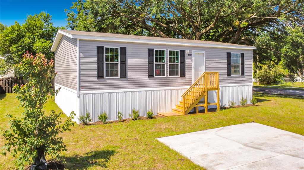 A light gray manufactured home with white skirting, black shutters, and wooden stairs — 8002 MOBILAIRE DRIVE, ORLANDO, FL