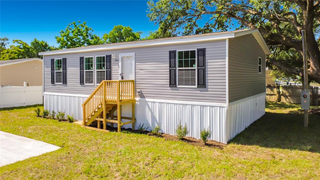 A gray manufactured home with white skirting and a wooden front porch sits on grass — 8002 MOBILAIRE DRIVE, ORLANDO, FL