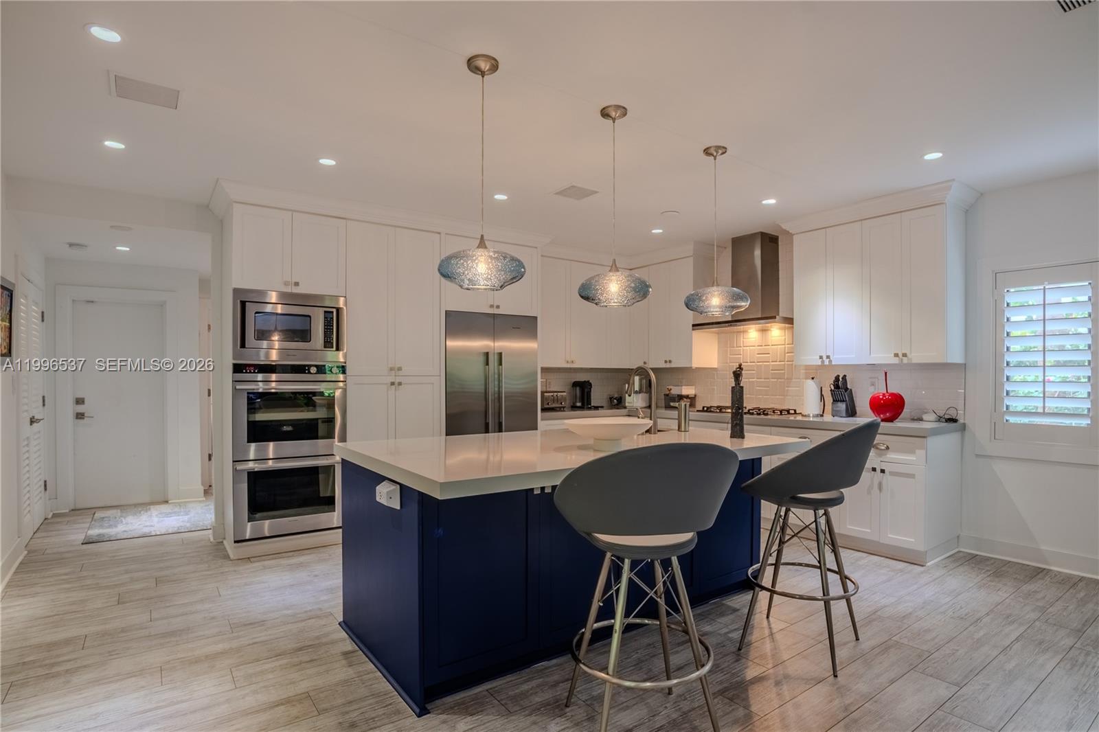 A kitchen features a blue island, white cabinetry, stainless steel appliances, and three glass pendants — 231 Fluvia Ave # 0, Coral Gables FL 33134, CORAL GABLES, FL