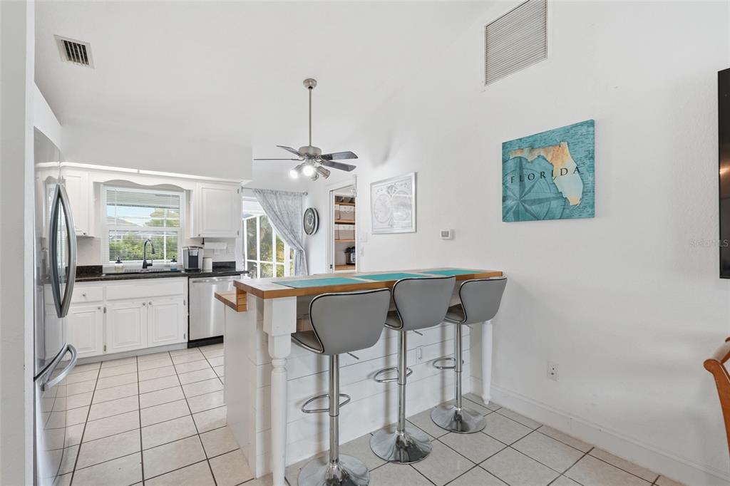 A kitchen features white cabinets, a wooden breakfast bar with three stools, and tile flooring — 25449 DOREDO DRIVE, PUNTA GORDA, FL