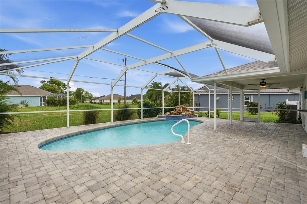A swimming pool with a rock water feature sits inside a screened-in patio area — 25449 DOREDO DRIVE, PUNTA GORDA, FL