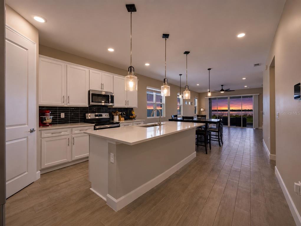 A modern kitchen with white cabinets, a quartz island, and a view of a sunset — 984 GRIFFON AVENUE, LAKE ALFRED, FL