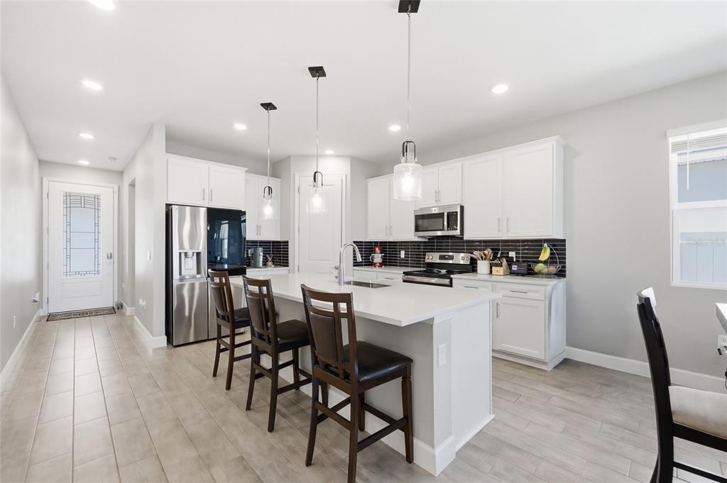 A modern kitchen features white cabinetry, a quartz-topped island with bar stools, and tiled floors — 984 GRIFFON AVENUE, LAKE ALFRED, FL