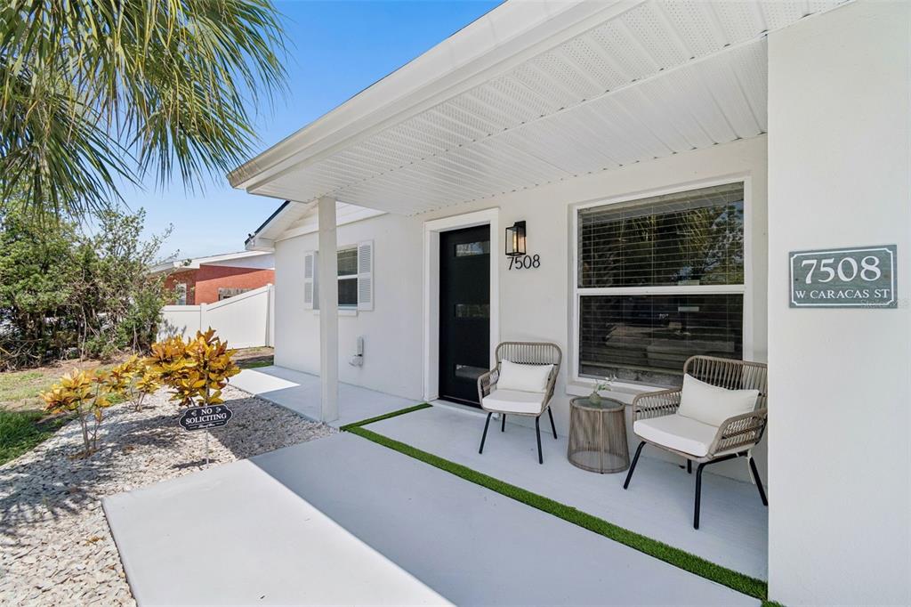 A covered front porch features a black door, two chairs, and a small side table — 7508 W CARACAS STREET, TAMPA, FL