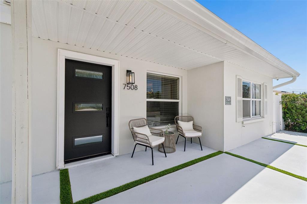 A modern front porch features a black door, two wicker chairs, and artificial grass accents — 7508 W CARACAS STREET, TAMPA, FL