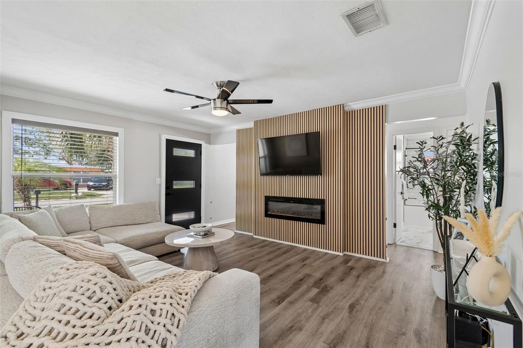 A living room features a wood-slat accent wall with a mounted television and electric fireplace — 7508 W CARACAS STREET, TAMPA, FL