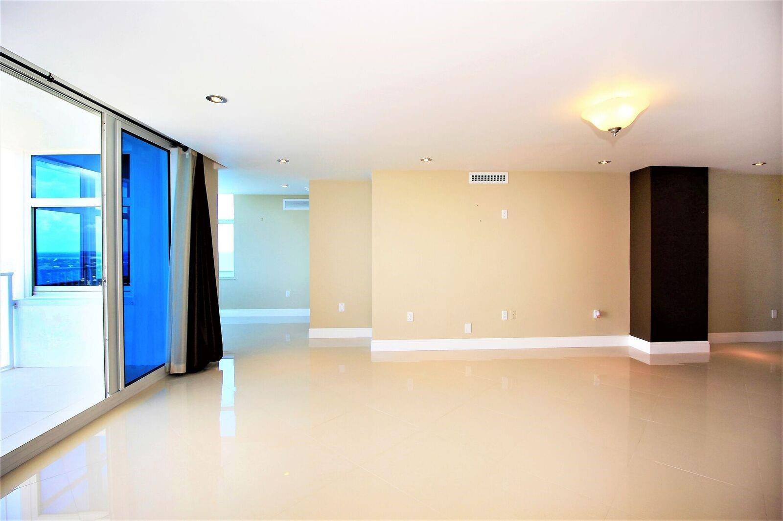 An empty living room with beige walls, light tile flooring, and a sliding glass door — 1360 S Ocean Boulevard # 2806, Pompano Beach FL 33062, POMPANO BEACH, FL