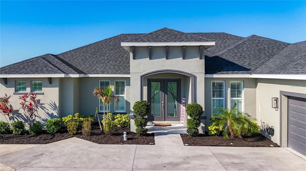The exterior of a single-story house features a concrete driveway, dark roof, and double doors — 5216 LAKE VENICE DRIVE, WIMAUMA, FL