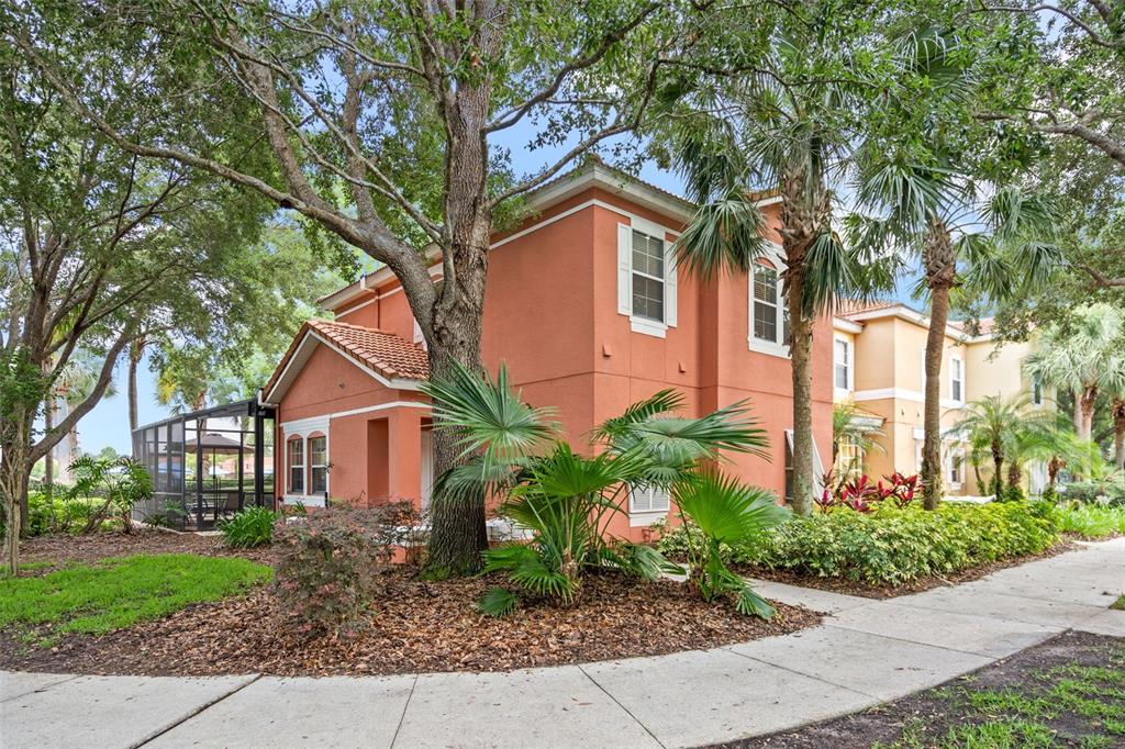 A two-story orange stucco townhouse with a screened-in patio and surrounding palm trees — 3015 YELLOW LANTANA LANE, KISSIMMEE, FL