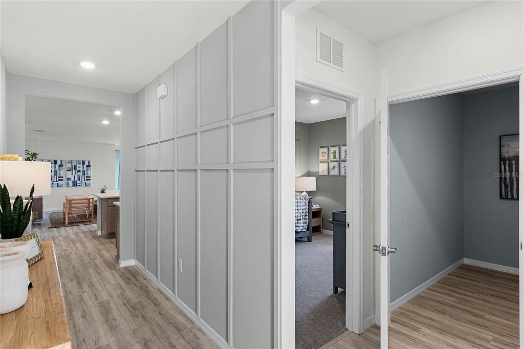 A hallway with light wood flooring and a gray paneled wall leads to other rooms — 7851 FORREST FOX WAY, LAKELAND, FL