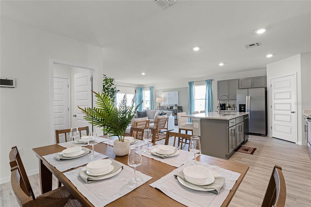 A dining area with a wooden table leads into an open-concept kitchen and living room — 7851 FORREST FOX WAY, LAKELAND, FL