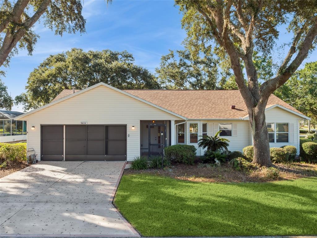 A single-story house with light siding, a two-car garage, and a large tree in front — 5616 LAVER STREET, LEESBURG, FL