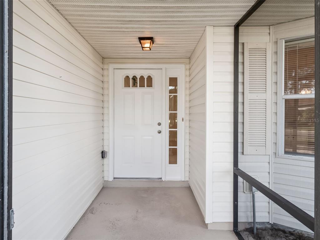 A covered entryway features white horizontal siding, a white front door with glass panels, and a window — 5616 LAVER STREET, LEESBURG, FL