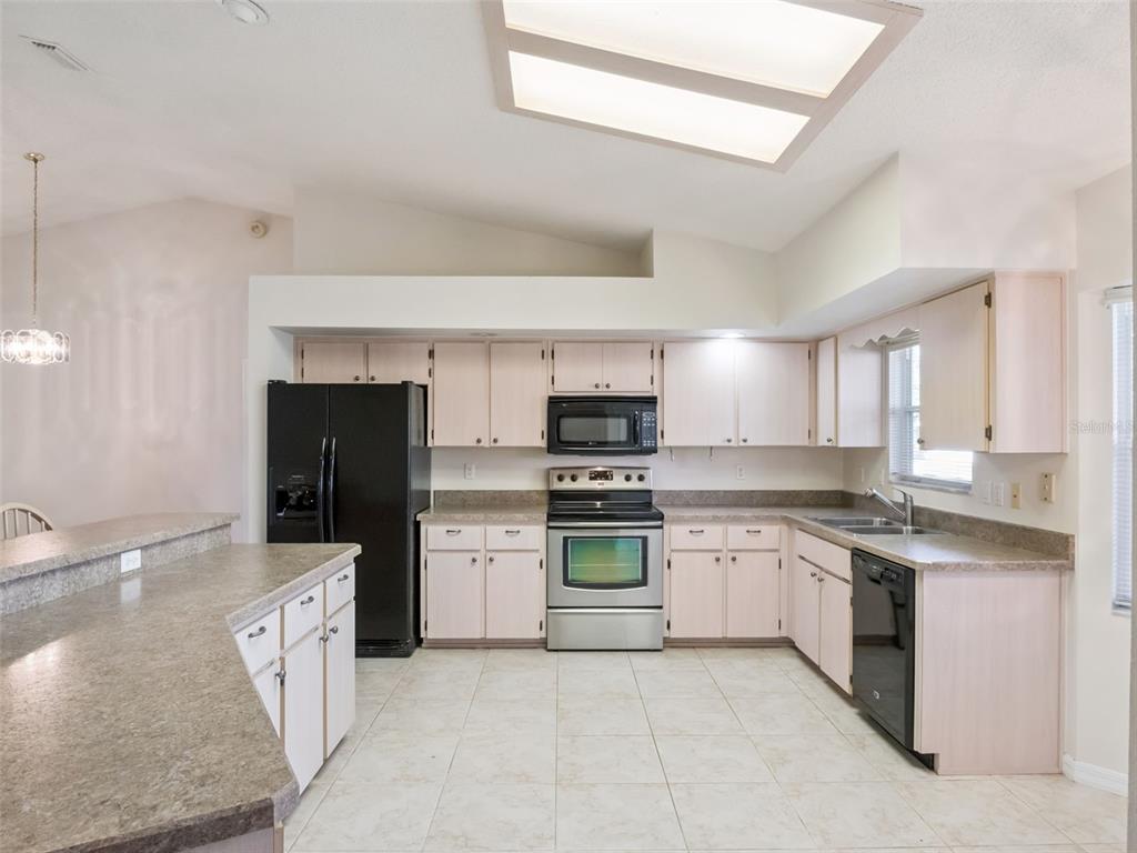 A kitchen with light cabinets, laminate countertops, stainless steel appliances, and a black refrigerator — 5616 LAVER STREET, LEESBURG, FL