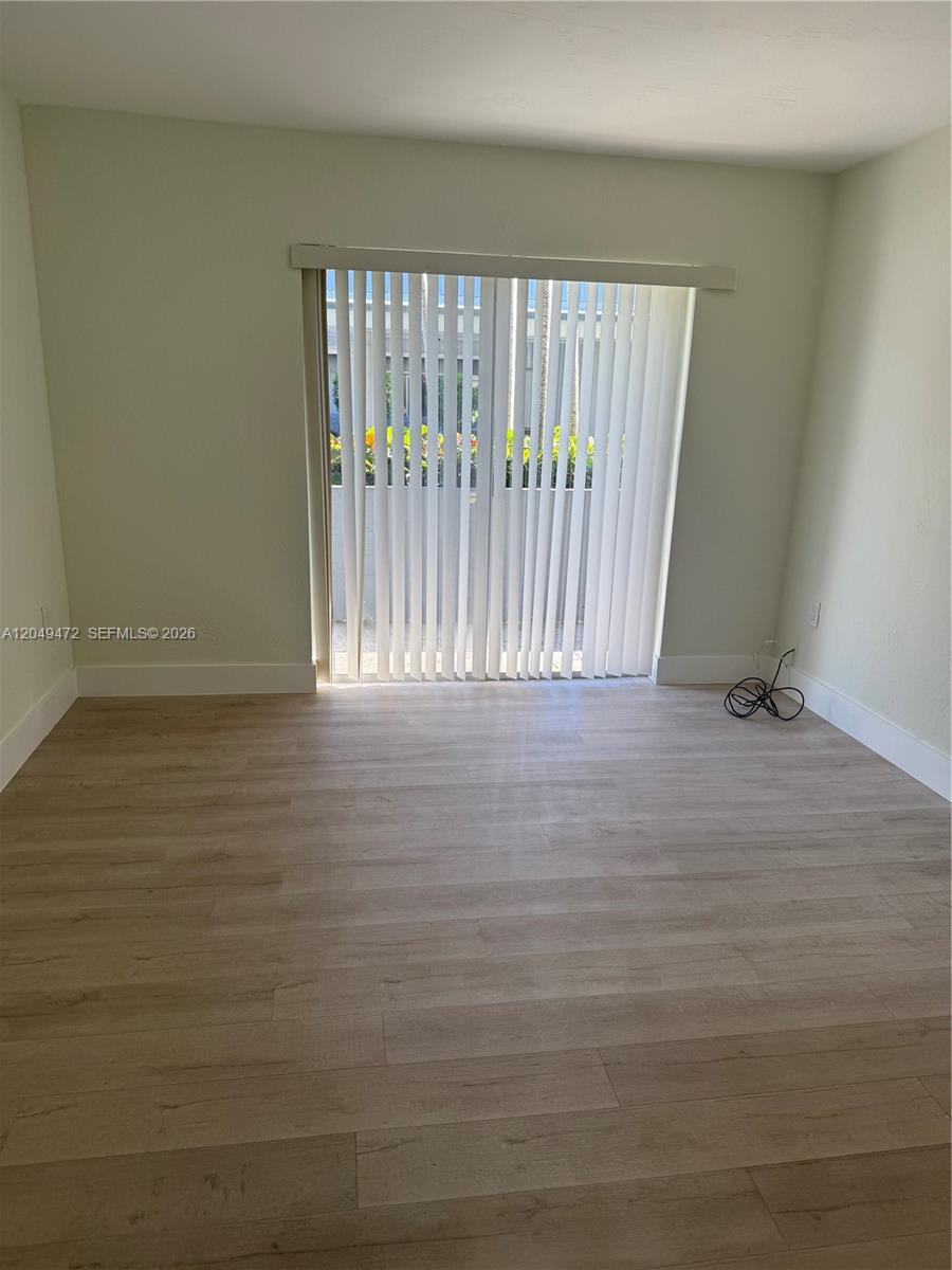 An empty room features light wood-look flooring, pale walls, and vertical blinds over sliding doors — 7403 SW 82nd St # 109N, Miami FL 33143, MIAMI, FL
