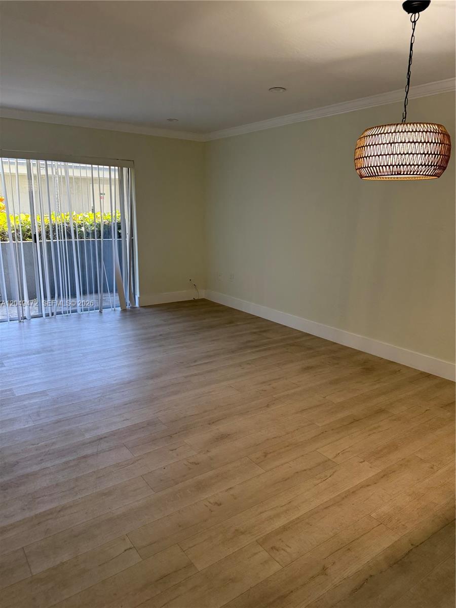 An empty room features light wood-look flooring, pale walls, and a hanging woven light fixture — 7403 SW 82nd St # 109N, Miami FL 33143, MIAMI, FL