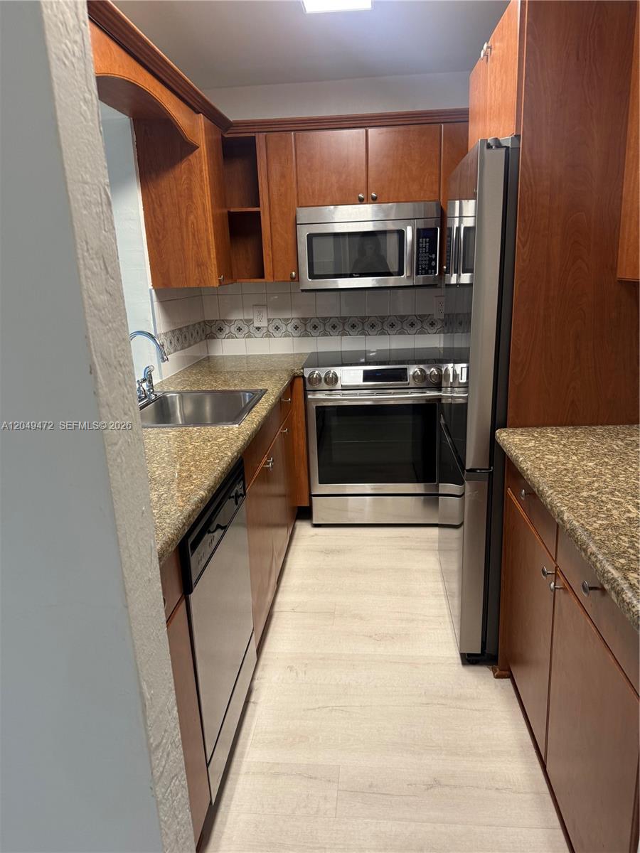 A galley kitchen features wood cabinets, granite countertops, and stainless steel appliances — 7403 SW 82nd St # 109N, Miami FL 33143, MIAMI, FL