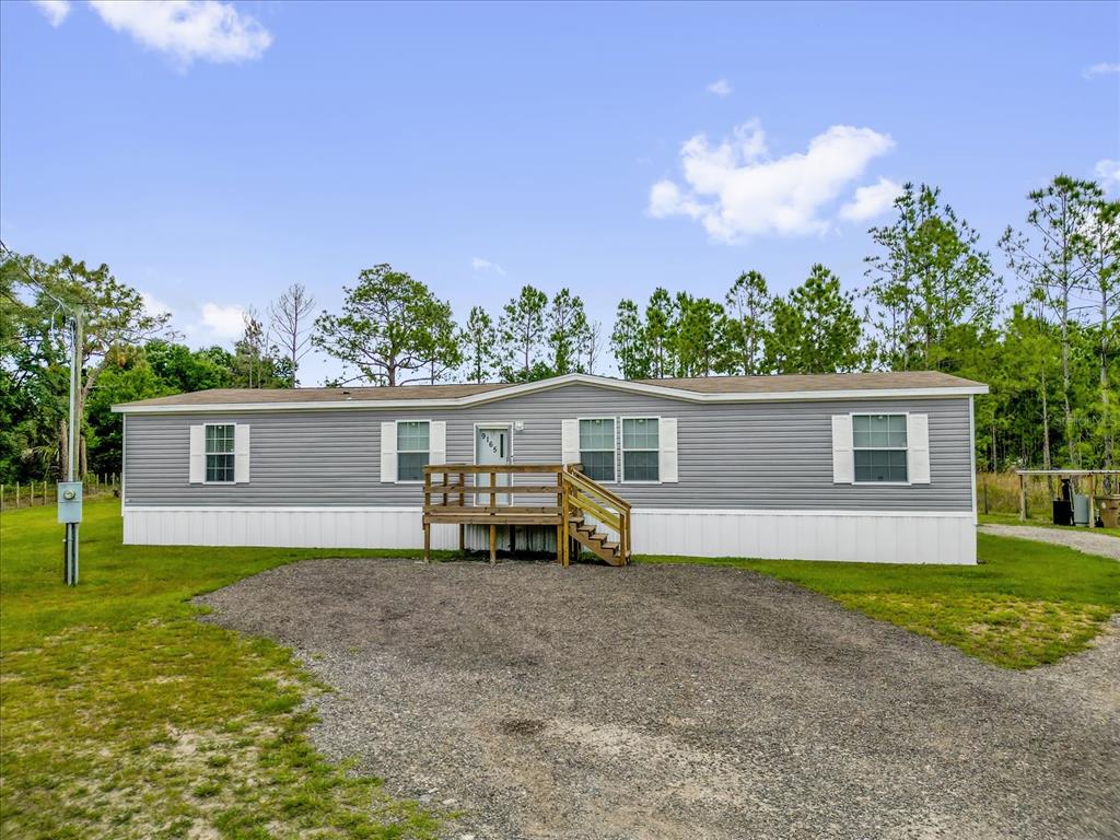 A gray manufactured home with white skirting and a wooden front porch sits on gravel — 9165 LUNA DRIVE, ST CLOUD, FL