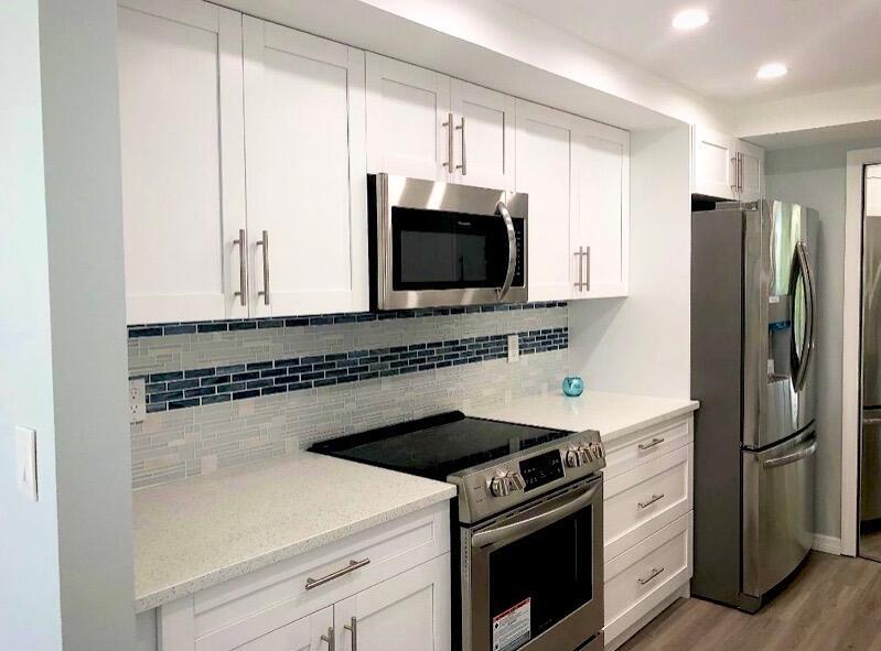 A kitchen features white cabinets, stainless steel appliances, and a blue and white tiled backsplash — 859 Jeffery Street # 311, Boca Raton FL 33487, BOCA RATON, FL
