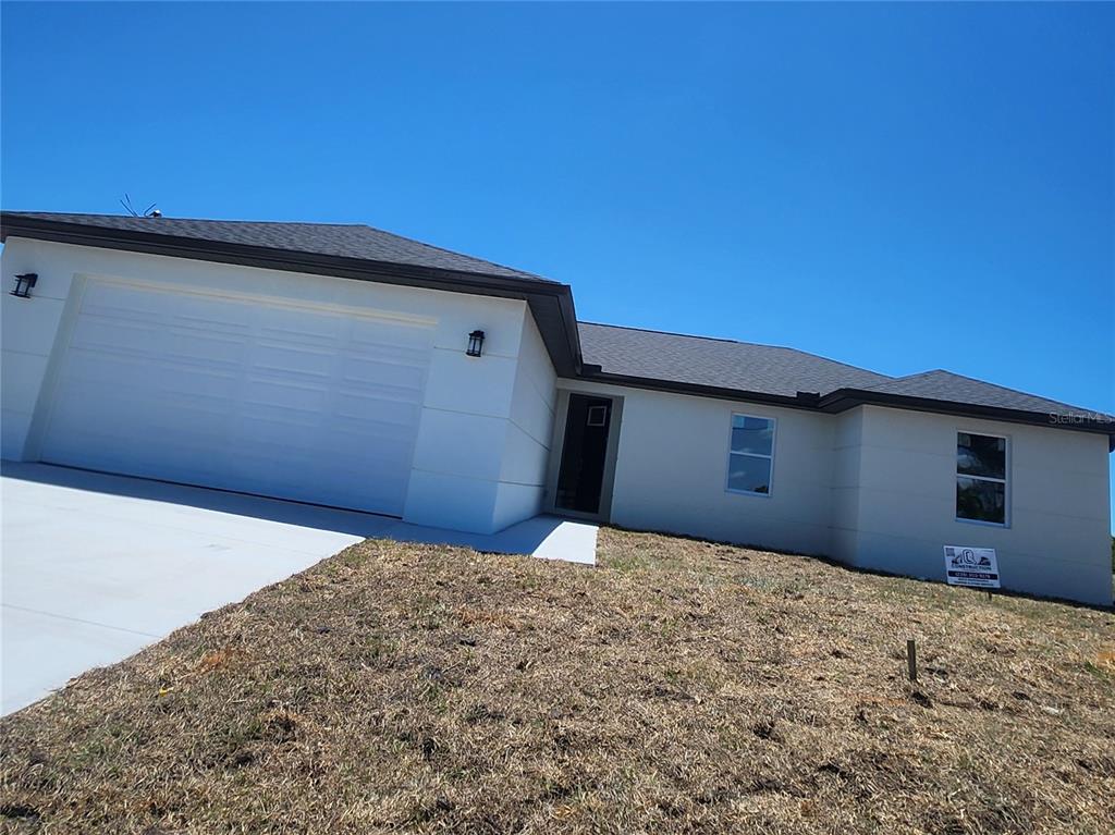 A single-story house with a white exterior, a two-car garage, and a sloped, grassy yard — 12025 CLARENDON AVENUE, PORT CHARLOTTE, FL
