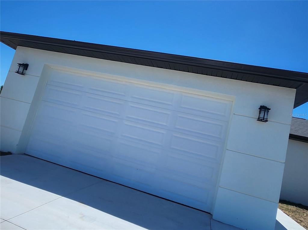 A white two-car garage door is set into a modern home exterior with dark trim — 12025 CLARENDON AVENUE, PORT CHARLOTTE, FL