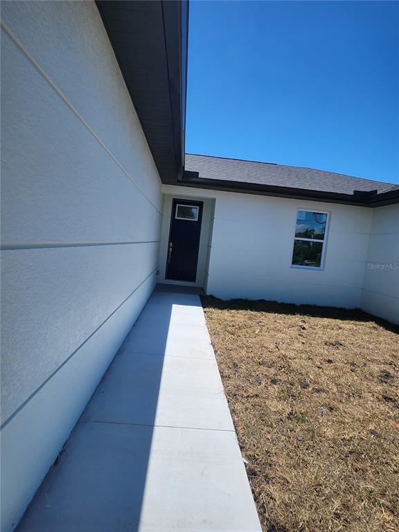 A concrete walkway leads to the dark front door of a white stucco house — 12025 CLARENDON AVENUE, PORT CHARLOTTE, FL