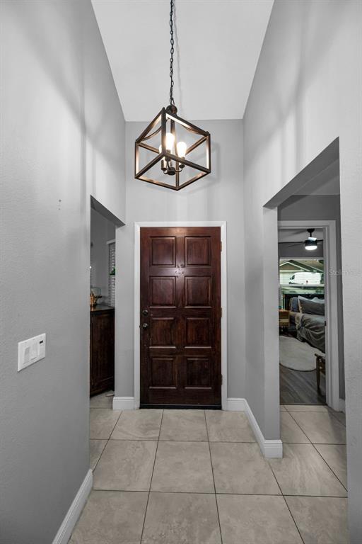An entryway with a dark wood door, tile flooring, and a geometric pendant light fixture — 11916 SNAPDRAGON ROAD, TAMPA, FL