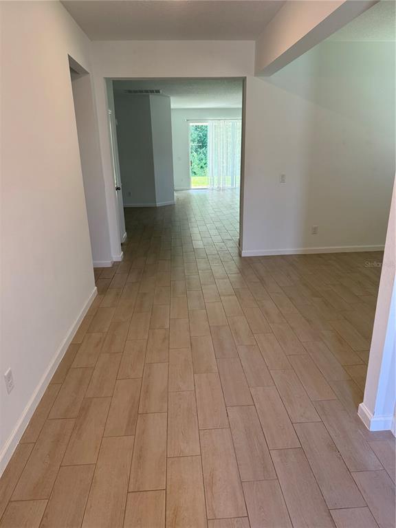 A hallway with light wood-look tile flooring leads toward a room with a sliding glass door — 5089 GRAND TETON COURT, DELAND, FL