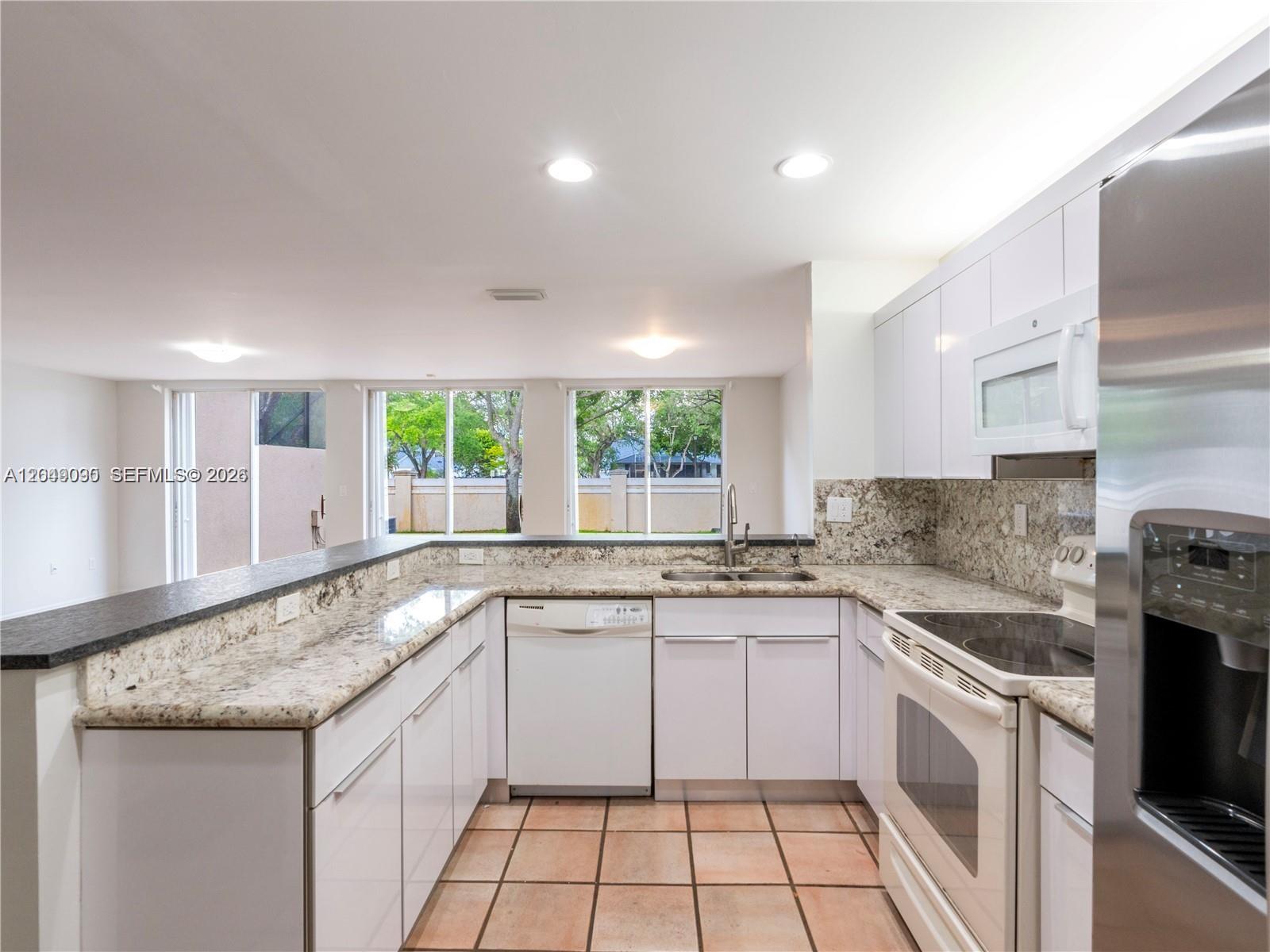 A kitchen features white cabinets, granite countertops, a stainless steel refrigerator, and tiled flooring — 5243 NW 102nd Ct # 5243, Doral FL 33178, DORAL, FL