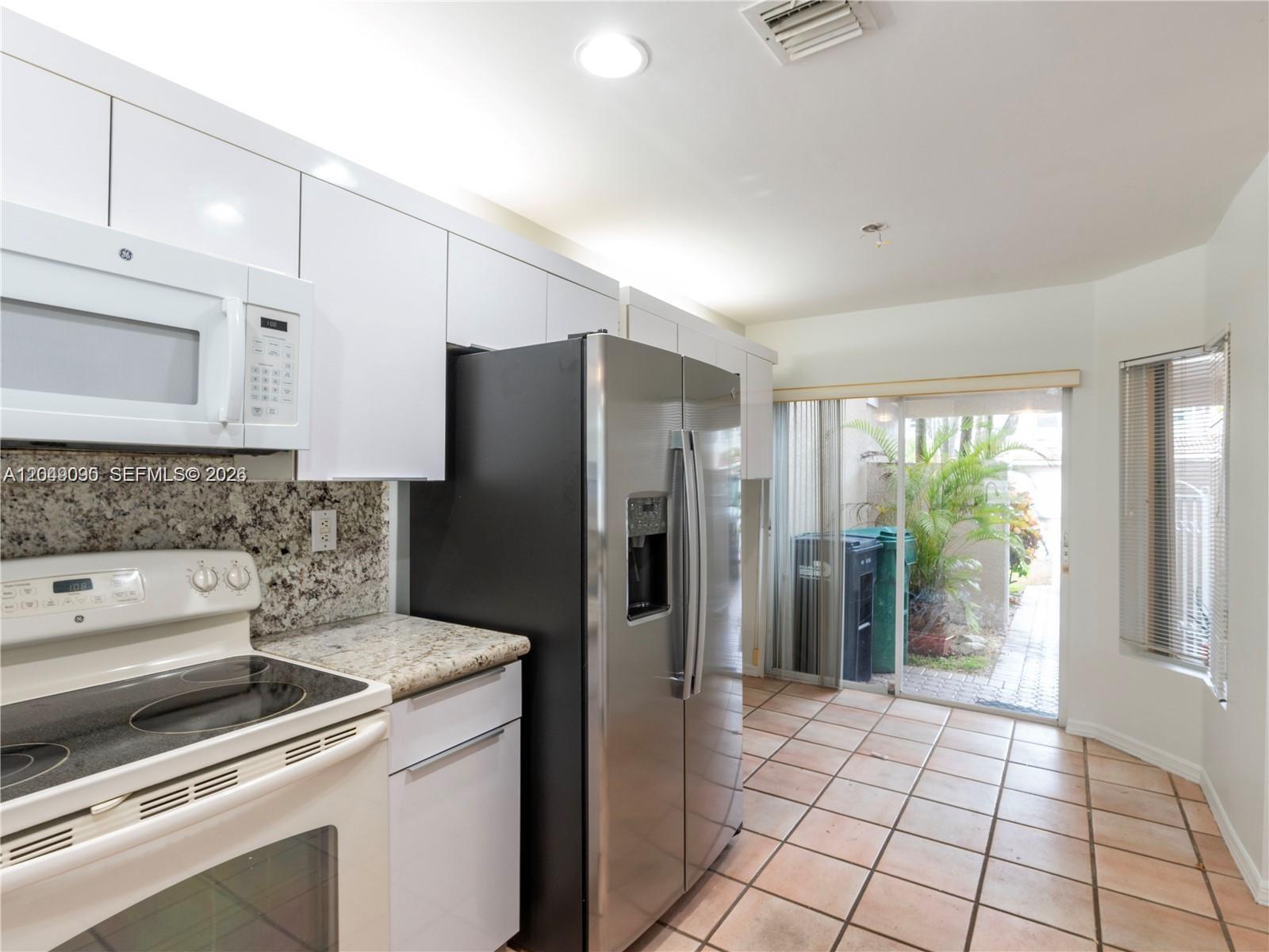 A kitchen features white cabinets, stainless steel appliances, granite countertops, and a sliding glass door — 5243 NW 102nd Ct # 5243, Doral FL 33178, DORAL, FL