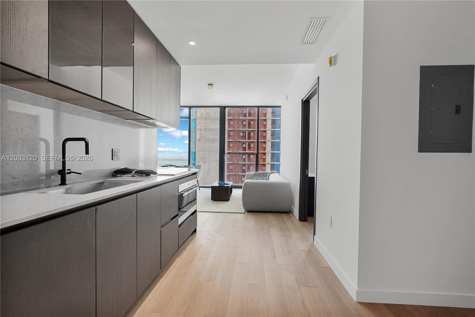 A modern kitchen with dark cabinetry and white countertops opens into a living area — 20 NE 11th St # 4006, Miami FL 33132, MIAMI, FL