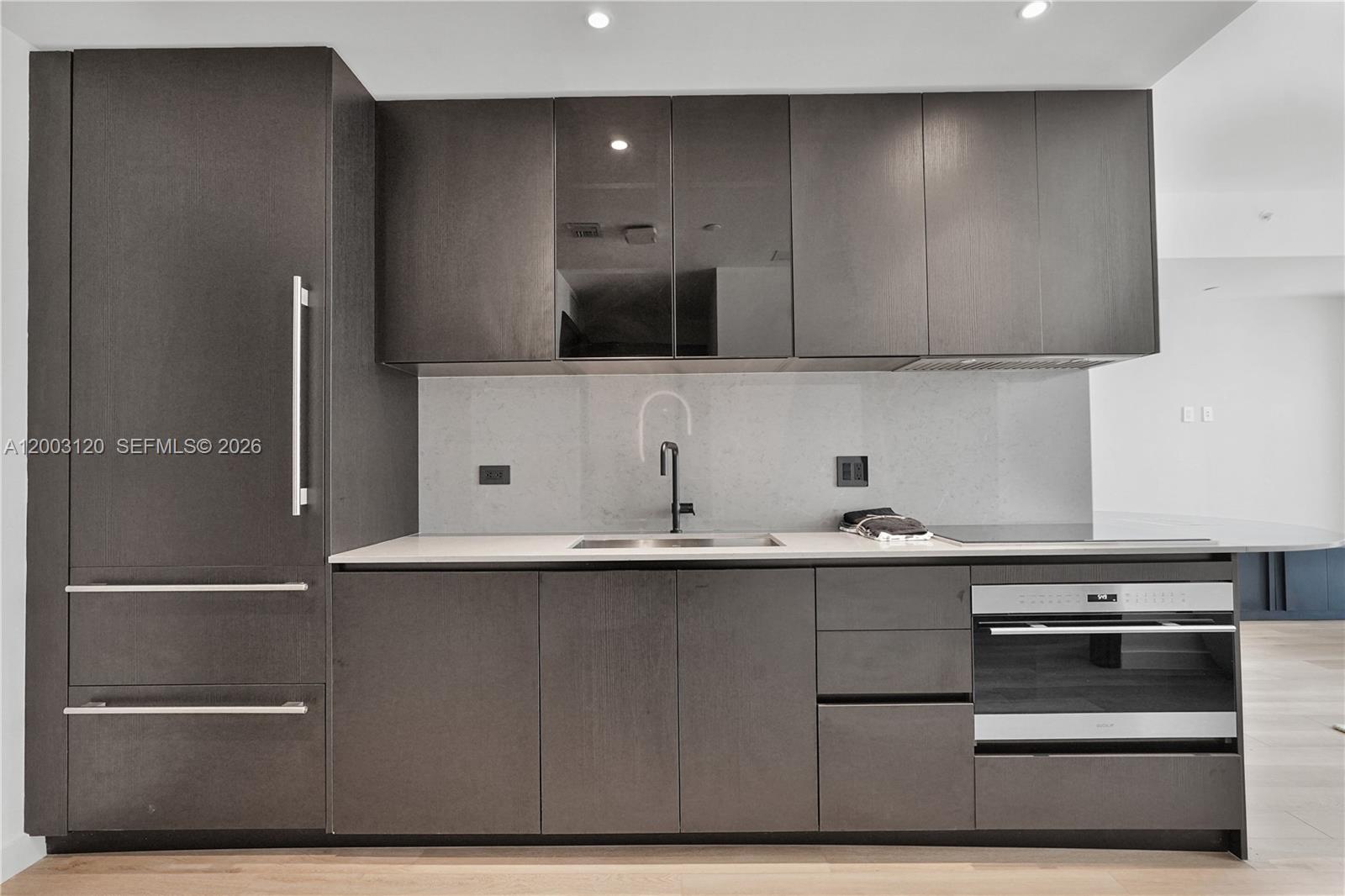 A modern kitchen features dark wood cabinetry, a light stone countertop, and integrated stainless appliances — 20 NE 11th St # 4006, Miami FL 33132, MIAMI, FL
