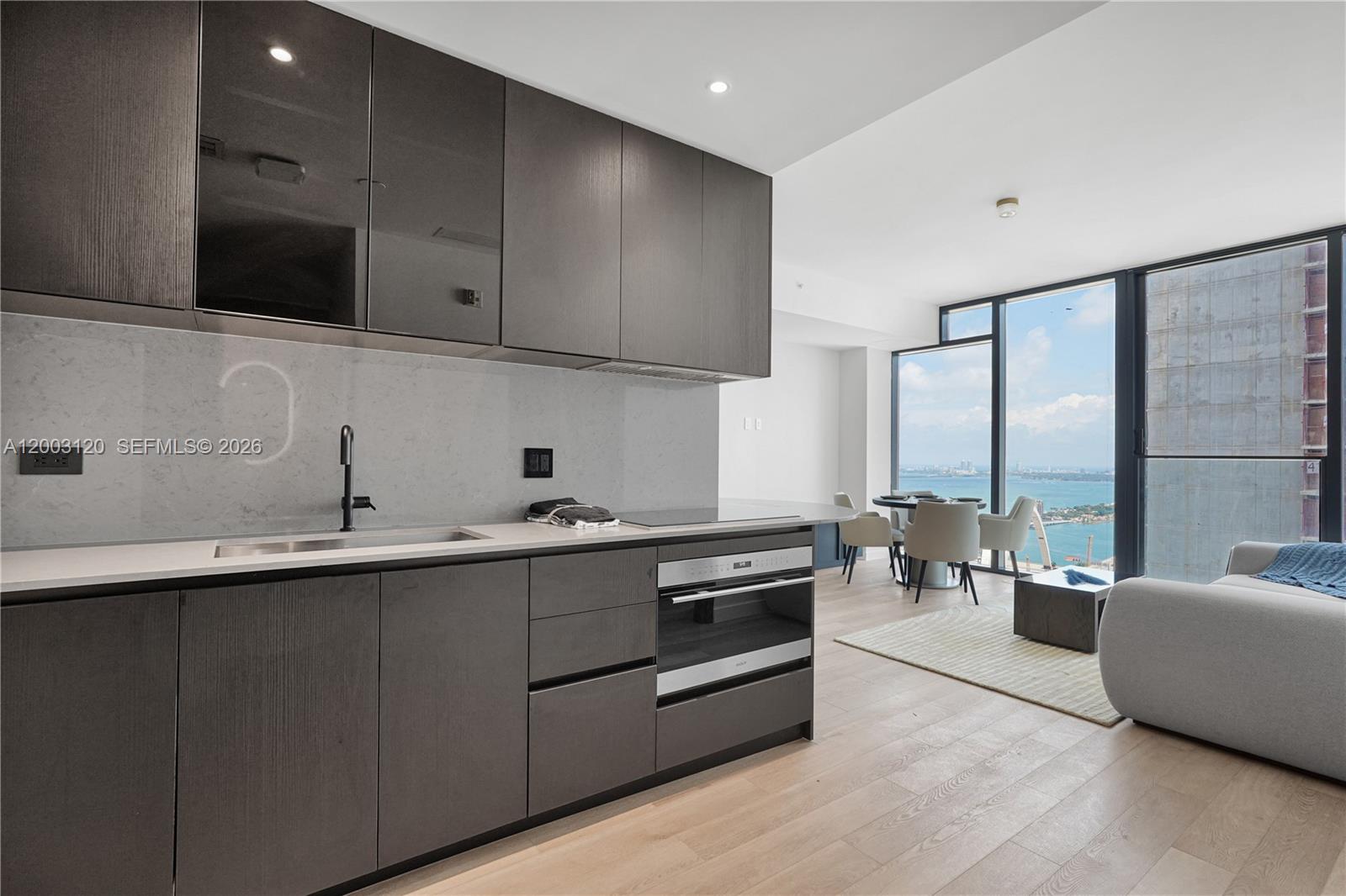 A modern kitchen with dark cabinetry and white countertops overlooks a dining area and ocean — 20 NE 11th St # 4006, Miami FL 33132, MIAMI, FL