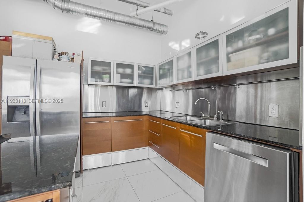 A kitchen features stainless steel appliances, wood cabinets, a black countertop, and a metal backsplash — 10 SW South River Dr # 608, Miami FL 33130, MIAMI, FL