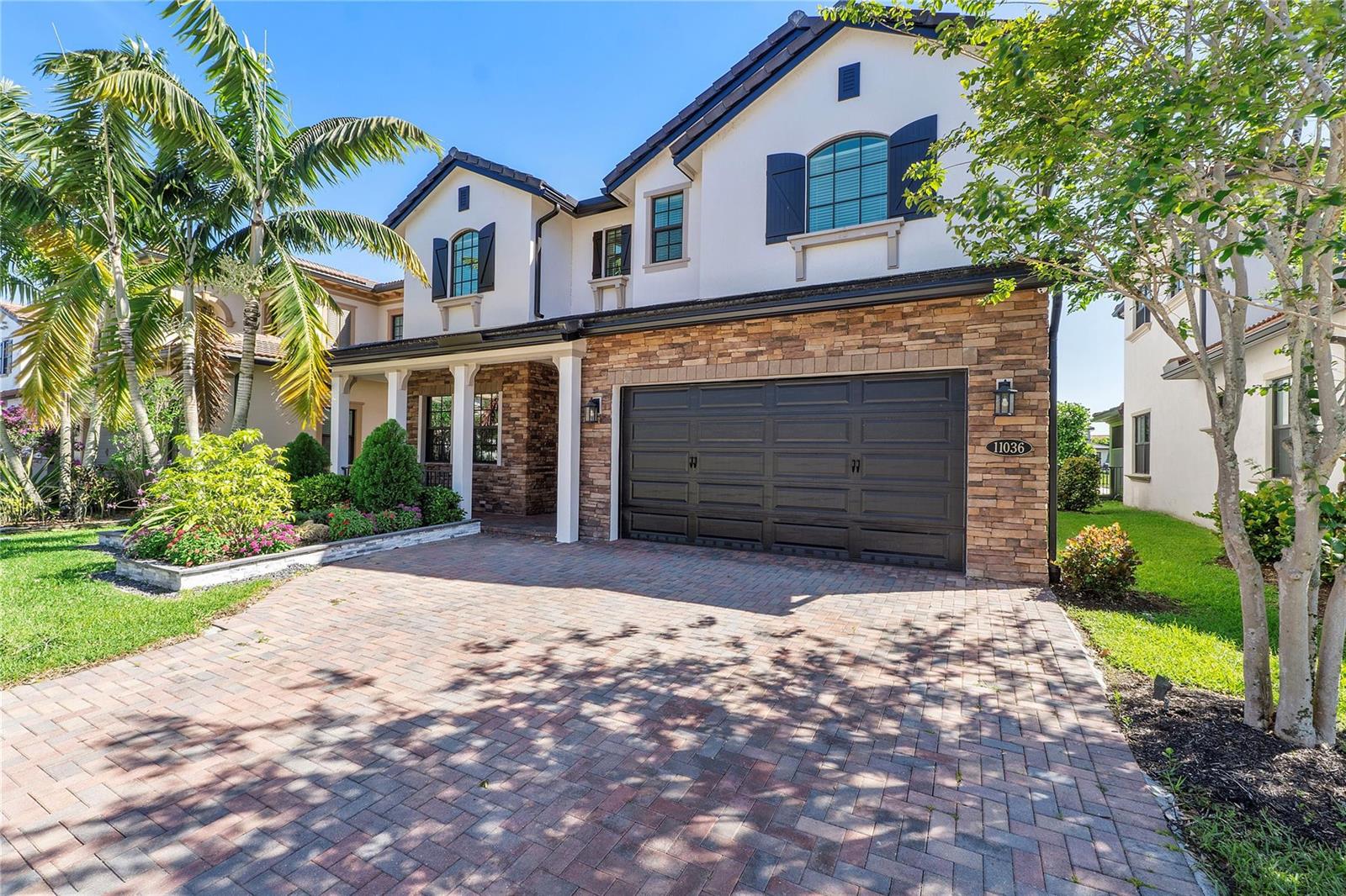 A two-story house with a stone facade, a dark garage door, and a brick driveway — 11036 Meridian Drive N, Parkland FL 33076, PARKLAND, FL