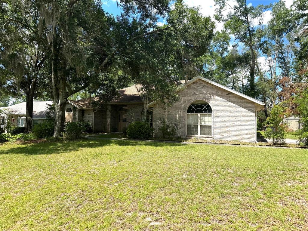 A single-story brick house with a large arched window sits behind a grassy lawn — 571 NW ZACK DRIVE, LAKE CITY, FL